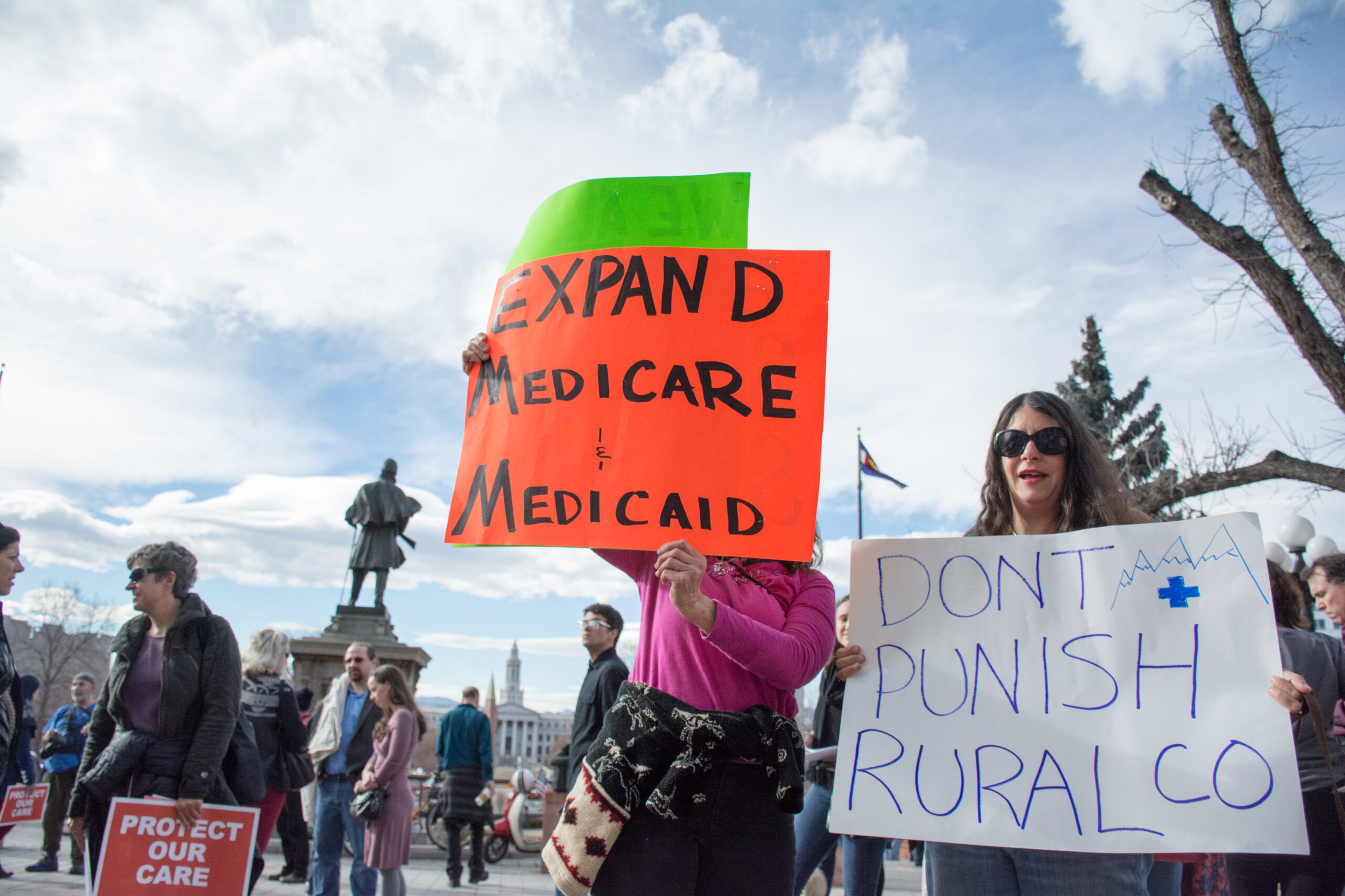 Protestor holding a sign that says expand medicare and medicaid out the Colorado capitol building. 
